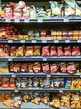 Kiel, Almanya - 19. Nisan 2025: Bir süpermarketin raflarını dolduran çeşitli cips ve abur cuburlar, tüketicilere sunulan ürünlerin çeşitliliğini gösteriyor