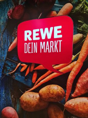 Kiel, Almanya - 19. Nisan 2025: REWE Dein Markt logosunu çevreleyen taze sebzeler sağlıklı yeme ve yerel üretimi teşvik etmektedir
