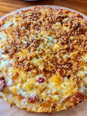 Erimiş peynir ve kızarmış soğanla kaplı iştah açıcı pizzanın yakın çekimi ahşap bir kesme tahtasının üzerinde servis edilerek görsel olarak çekici bir mutfak sahnesi oluşturuldu.