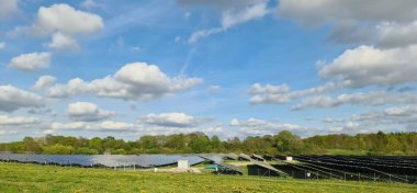 Fotovoltaik paneller büyük bir alanda güneş ışığını yakalıyor, kısmen bulutlu bir gökyüzü altında sürdürülebilir bir gelecek için temiz enerji üretiyor