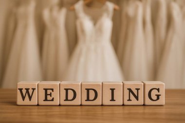 Üzerinde siyah harfler olan tahta küplerle arka planda bulanık gelinlikler asılı ahşap bir masada düğün yazılıydı.