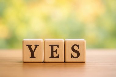Evet sözcüğünü oluşturan üç tahta küp, yumuşak bulanık doğal bir arka planla tamamlanmış, ahşap bir masada dinleniyor.