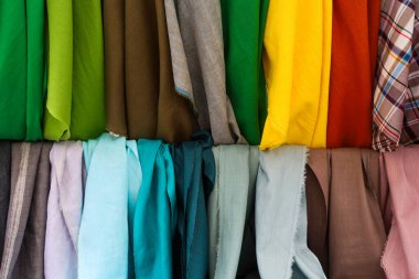 Canlı bir tekstil dükkanında asılı renkli kumaşlar, çeşitli giyim ve tasarım projeleri için terziler tarafından seçime davet ediliyor.