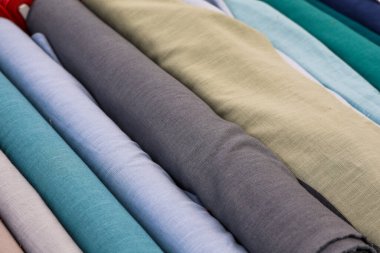 Renkli kumaş ruloları farklı doku ve renkleri sunar, moda, döşeme ve iç tasarım projeleri için idealdir.