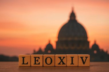 Tahta alfabe blokları gün batımında arka planda Aziz Peter Bazilikası ile 14. Leo heceleniyor.