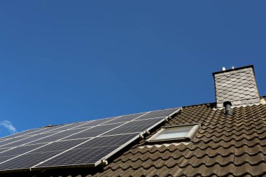 Fotovoltaik paneller, temiz ve sürdürülebilir enerji sağlayan açık mavi gökyüzüne karşı tavan penceresi ve bacası olan bir çatıya kurulur.