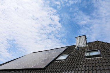 Çatıya baca ve tavan pencereleri olan fotovoltaik paneller yerleştirilmiş, sürdürülebilir enerji üretimi için güneş enerjisinden faydalanılıyor