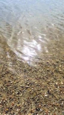 Saf suda parlayan güneş ışığı, yumuşak çakıl taşlarının üzerinde yavaşça akan, büyüleyici yansımalar ve şeffaf yüzey dokuları yaratır.