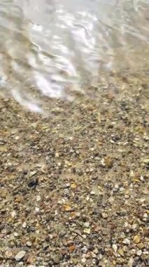 Çakıl taşları dalgalı suyun altında yavaş yavaş kayboluyor, uzak kıyıları ve rüzgar türbinleri olan sakin bir gölü ortaya çıkarıyor.