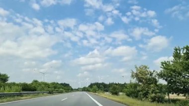 Asfalt yol yeşil ağaçlar ve mavi gökyüzünün altında rüzgar türbinleriyle çevrili ve Almanya 'da beyaz bulutlar var.