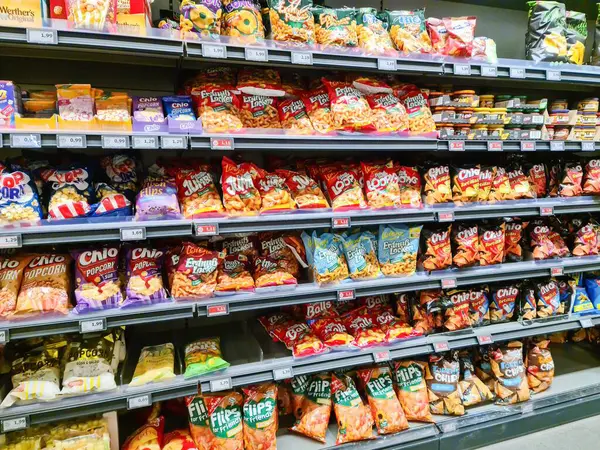 Kiel, Almanya - 28. Mayıs 2025: Almanya 'nın Kiel kentindeki bir süpermarkette renkli cips, patlamış mısır ve diğer atıştırmalıklarla dolu raflar