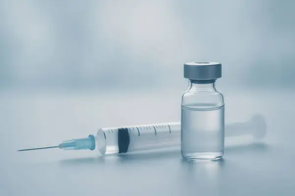 Aşıyla dolu şırınga ve şişe masada dinleniyor, yaklaşan enjeksiyon için hazırlanıyor, gerekli sağlık hizmetlerini vurguluyor.