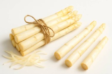 Taze beyaz kuşkonmaz mızrakları sicimle sarmalanmış, bazıları soyulmuş ve bir bütün olarak temiz beyaz arka planda sergilenmiş, aşçılık kullanımına hazır.