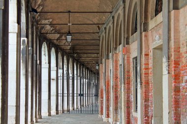 Venedik, İtalya - 24 Mayıs 2024: Metal kapıları ve tuğla duvarları olan boş kemerli geçit, tavandan sarkan lambalarla aydınlatılmış