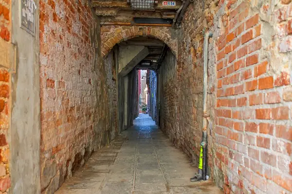 Venedik, İtalya - 24 Mayıs 2024: Venedik, İtalya 'da daha parlak bir alana açılan tuğla duvarlı dar geçit