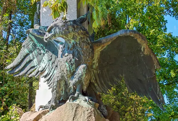 Venedik, İtalya - 24 Mayıs 2024: Bereketli yeşilliklerle çevrili, halka açık bir parktaki bir anıtın parçası olan kayanın üzerinde kanatları açık bronz kartal