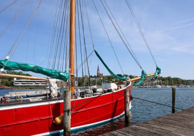 Flensburg, Almanya - 13. Haziran 2025: Güneşli yaz gününde Flensburg limanına demirlemiş yeşil yelkenli geleneksel kırmızı yelkenli gemi