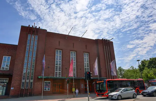 Flensburg, Almanya - 13. Haziran 2025: Almanya 'nın Flensburg kentinde yükselen Alman Haus, dalgalanan bayraklar ve hareketli şehir trafiğinin yanı sıra tuğla bir cephede yer alıyor