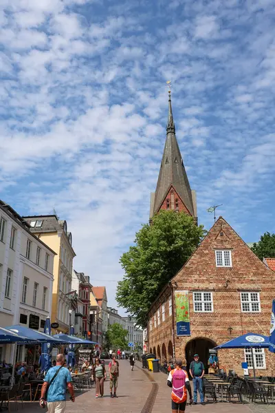 Flensburg, Almanya - 13. Haziran 2025: Arka planda Nordertorzwilling kilisesi yükselirken, Flensburg 'un eski kasabasında Rote Strae boyunca yürüyen insanlar 