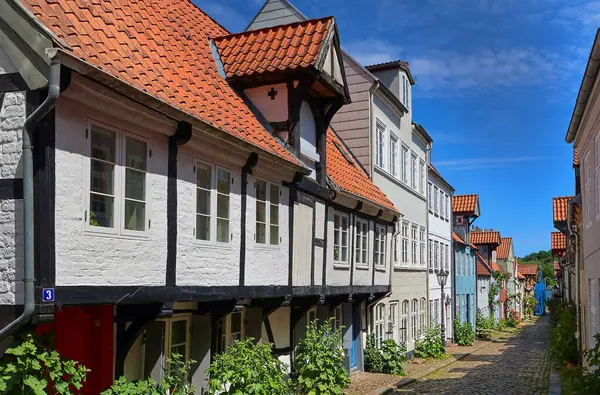 Flensburg, Almanya - 13. Haziran 2025: Geleneksel yarı keresteli evler, Almanya 'nın Flensburg kentinde parlak güneşli gökyüzü altında tarihi kentsel manzaraları sunan kaldırım taşı caddesinde sergileniyor