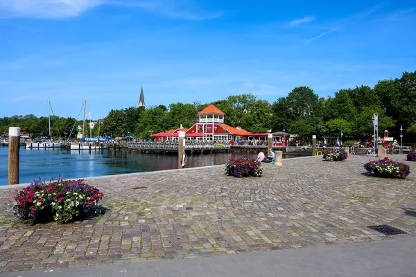 Flensburg, Almanya - 13. Haziran 2025: Almanya 'nın Flensburg kentindeki liman manzarasında güneşli bir yaz gününde tekneler, kırmızı bir restoran ve çiçek açılır.