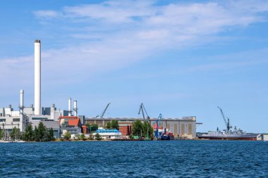 Almanya 'daki Flensburg limanı. Endüstriyel binalar, vinçler, tersaneler ve güzel bir yaz gününde mavi gökyüzünün altında bazı bulutlarla kenetlenmiş gemiler.
