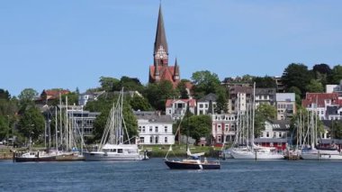 Flensburg, Almanya - 13. Haziran 2025: Christuskirche kilisesi ve güneşli bir yaz gününde yelkenli tekneleriyle Flensburg limanının güzel manzarası