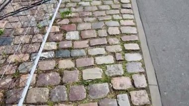 Taşlar arasında yemyeşil çimlerin filizlendiği, karmaşık yüzey dokuları ve doğal büyüme kalıplarıyla pürüzsüz asfalt bir yol çevreleyen yıpranmış kaldırım taşı kaldırımı