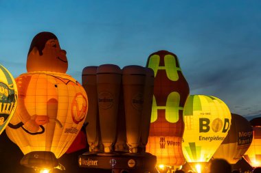 Kiel, Almanya - 21. Haziran 2025: Kiel Haftası boyunca alacakaranlıkta parlayan çeşitli şekillere ve marka logolarına sahip aydınlık sıcak hava balonları, canlı bir görüntü yarattı