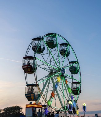 Kiel, Almanya - 21. Haziran 2025: Güneşin batışında parlayan renkli kamaraları ve yıldızlarla aydınlatılmış dönme dolap