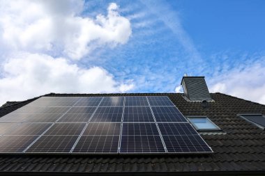 Fotovoltaik paneller çatıya kurulur, parçalı bulutlu bir gökyüzünün arka planına karşı güneş ışığından temiz enerji üretirler.