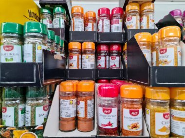 Kiel, Almanya - 18. Haziran 2025: Turuncu, kırmızı ve yeşil kapaklı küçük plastik kavanozlardaki renkli baharatlar ve otlar, karaborsa raflarında sergileniyor