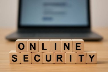 Arkaplanda internet güvenliği ve korunmasını temsil eden bir dizüstü bilgisayarla çevrimiçi güvenlik kelimelerini oluşturan tahta küpler.