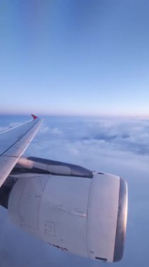 Uçak türbini, hava yolculuğu sırasında kanadı çevreleyen parlak günbatımı renkleriyle pofuduk bulut katmanının üzerinde dönüyor.