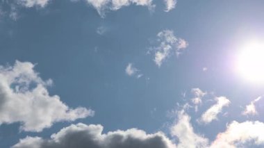 Sıcak güneş ışığı tüylü kümülüs bulutlarına nüfuz ediyor, dingin gündüz koşullarında parlak bir ışık saçan, geniş mavi gökyüzünü aydınlatıyor.