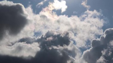 Sıcak güneş ışığı tüylü kümülüs bulutlarına nüfuz ediyor, dingin gündüz koşullarında parlak bir ışık saçan, geniş mavi gökyüzünü aydınlatıyor.