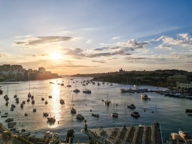 Malta, Valletta - 29. Eylül 2024: Valletta limanını aydınlatan altın gün batımı, Akdeniz cazibesiyle tarihi şehir manzarasına karşı demirlemiş tekneleri sergiliyor
