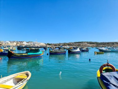 Malta, Valletta - 29. Eylül 2024: Valletta 'nın canlı mavi gökyüzü altında turkuaz sularda sallanan renkli luzzu tekneleri