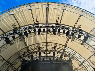 Sahne ışıklarının düşük açılı görüntüsü ve mavi gökyüzü altında açık hava müzik festivalinin tuval destekleyici çatısı.
