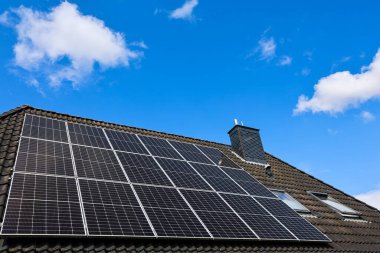 Fotovoltaik paneller, açık mavi gökyüzü altında sürdürülebilir enerji üretimi için güneş enerjisini kullanan fayanslı bir çatıya kurulur.