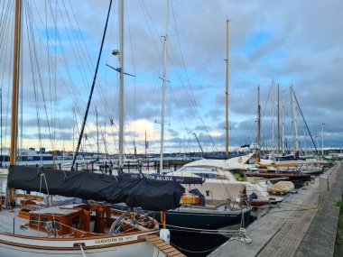 Kiel, Almanya - 02. Ağustos 2025: Lüks yelkenliler ve yatlar, bulutlu bir gökyüzü altında bir sonraki yolculuklarını beklerken modern bir marinada demirlediler.