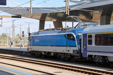 Viyana, Avusturya - 10. Temmuz 2025: Avusturya 'daki Viyana Merkez İstasyonu' nda modern tepe örtüsü altında mavi ve gümüş elektrikli lokomotif yolcu trenini çekiyor