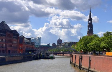 Hamburg, Almanya - 23. Ağustos 2025: Hamburg 'dan akan Elbe Nehri manzarası, bulutlu bir gökyüzü altında geleneksel binalar, Elbphilharmonie ve St. Katharinen Kilisesi' ni vurguluyor.