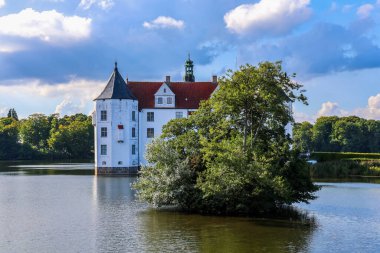 Gluecksburg, Almanya - 29. Ağustos 2025: Gluecksburg Şatosu güneşli bir günde ağaçlarla çevrili göle yansıyor