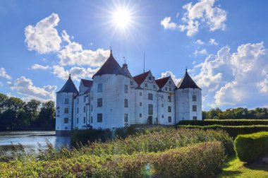 Gluecksburg, Almanya - 29. Ağustos 2025: Schloss Glcksburg Şatosu, güneşli bir günde bulutlar ve parlayan güneşle gölü yansıtıyor 