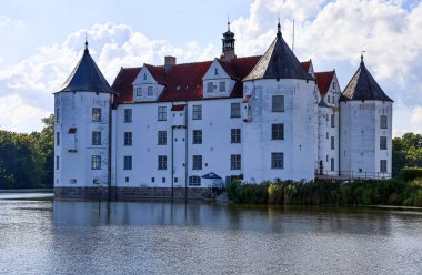 Gluecksburg, Almanya - 29. Ağustos 2025: Almanya 'daki Gluecksburg Şatosu bulutlu güneşli bir günde gölü yansıtıyor