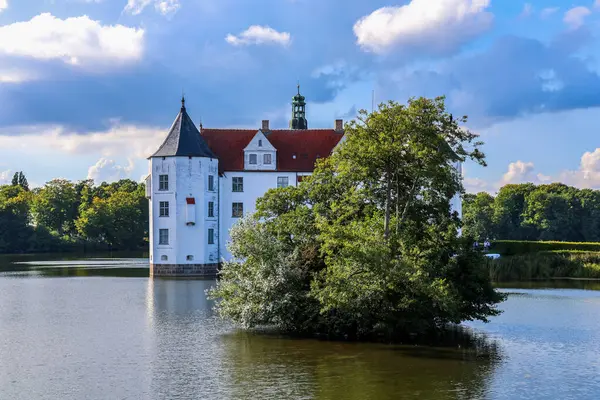 Gluecksburg, Almanya - 29. Ağustos 2025: Gluecksburg Şatosu güneşli bir günde ağaçlarla çevrili göle yansıyor