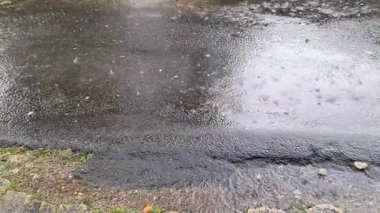 Heavy raindrops creating ripples and splashes on a wet asphalt road surface. Water flowing in a stream along the edge of the urban street
