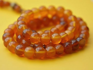 Kehribar boncuklar zarif sarı bir zemin üzerinde duruyor. Mücevherlerin güzelliğini ortaya çıkaran çarpıcı bir kontrast oluşturuyor.