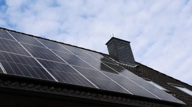Modern photovoltaic solar panels installed on a tiled house roof, generating clean and renewable energy as clouds move across the blue sky